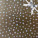 image of a square of wrapping paper, the paper is gold and features lots of solid white stars, in the centre of the gift wrap paper is a gold paper gift wrapping bow