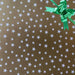 image of a square of wrapping paper, the paper is gold and features lots of solid white stars, in the centre of the gift wrap paper is a red paper gift wrapping bow