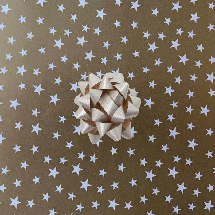 image of a square of wrapping paper, the paper is gold and features lots of solid white stars, in the corner of the gift wrap paper is a red gift wrapping bow